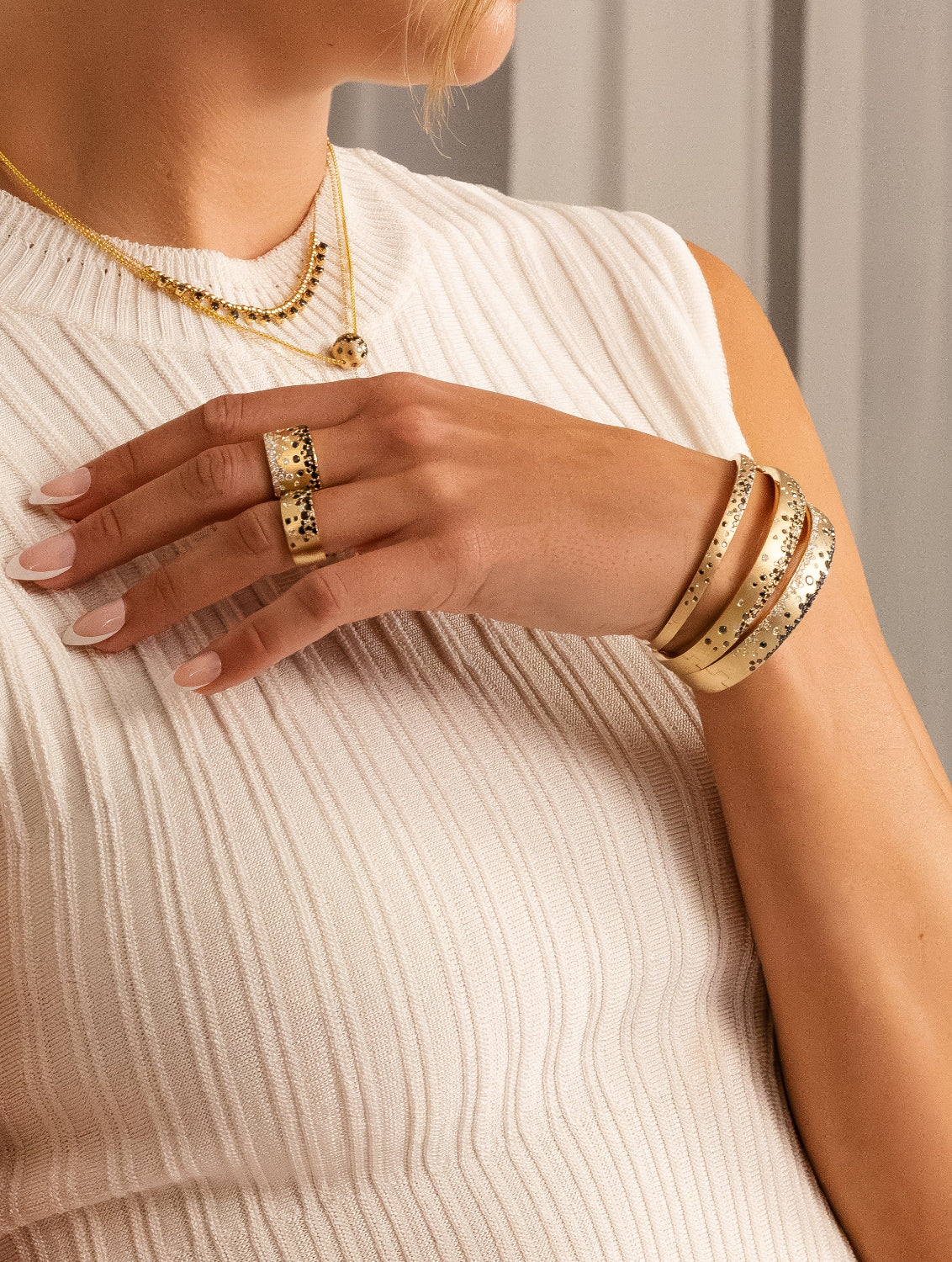 Close-up of a person wearing gold jewelry including rings and bracelets on a neutral background